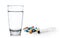 Glass of water syringe and colorful pill and capsules on white