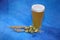 Glass of wheat beer with foam, hops and ears of corn on a blue background
