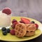 A glass of whipped cream, next to it are waffles with raspberries, blueberries and strawberries.