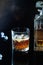 Glass of whiskey or bourbon with ice on black stone table. Glass of whiskey with ice and a square decanter. Glass of scotch