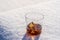 Glass of whiskey with ice on a bed of snow and white background, close up