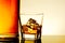 Glass of whiskey with ice cubes near bottle on table with reflection, warm tint atmosphere