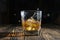 Glass of whiskey with ice cubes on a wooden table. An old tabletop with light and a glass of strong drink.