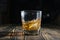 Glass of whiskey with ice cubes on a wooden table. An old tabletop with light and a glass of strong drink.