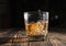 Glass of whiskey with ice cubes on a wooden table. An old tabletop with light and a glass of strong drink.