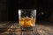 Glass of whiskey with ice cubes on a wooden table. An old tabletop with light and a glass of strong drink.