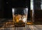 Glass of whiskey with ice cubes on a wooden table. An old tabletop with light and a glass of strong drink.