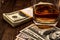 Glass of whiskey with pack of dollars on a wooden table.