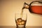 A glass of whiskey on the rocks. pouring Bourbon or cognac from a liquor bottle. orange background