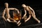 Glass of whisky and two mannequins on wooden table against black background. Alcoholism concept