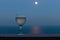 Glass of white wine on a balcony terrace with blurred blue sea on a full moon night.