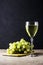 A glass of white wine and a brush of white grapes on a cutting board in the background on a black background