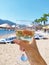 a glass of white wine in hand on the background of a sunny beach with sun loungers, umbrellas and palm trees