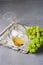 Glass of White Wine Lying on Napkin and Branch of Green Grapes on Gray Background Vertical