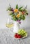 Glass of white wine, strawberries, grapes, a bouquet of flowers in a white jug on the table in the room. Delicious aperitif