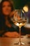 Glass of white wine on table on background of unrecognizable woman sitting in cafe or restaurant. Focus on wine glass