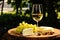 Glass of white wine, variety of cheese pieces, elegant wooden plate and luxurious atmosphere