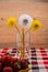 A glass with white and yellow dandelions, a plate with strawberries is on the table