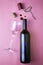 Glass wine bottle glass stopper corkscrew shrink cap and drops of red wine on pink background