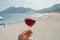 Glass of wine in hand. A glass of red wine against the background of the Mediterranean beach and the sea in a tourist