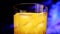 A glass with yellow-orange sweet multifruit juice and ice cubes