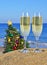 Glasses of champagne and Christmas tree on a beach
