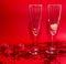 Glasses of champagne, red candles, red confetti in the shape of a heart on a red background