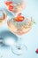 Glasses with cold pink champagne or punch with wine strawberries, ice and rosemary on blue background