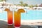 Glasses with colored cocktails on the side of a swimming pool