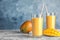 Glasses of fresh mango drink and fruits on table against color background
