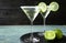 Glasses of Lime Drop Martini cocktail on light blue wooden table against dark background