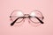 Glasses in round thin metal frame isolated on pink surface.