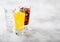 Glasses of soda drink with ice cubes and bubbles on stone kitchen table background. Cola and orange lemonade soda