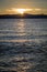 Glassy water with the golden sun setting behind flat mountains in the distance looking from Lakeside Beach at Lake Tahoe