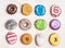 Glazed colorful doughnuts with sprinkles and icing on white wooden background, top view