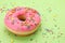 Glazed donut decorated with sprinkles on green background, closeup. Space for text. Tasty confectionery