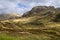 The Glen Coe valley shines with verdant slopes under sunlight, shadowed areas, and a trail winding through the Highlands