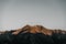 gloomy bare treeless mountains with snow capped top and summit lit by sunset sunlight under gray sky, arthur pass, new