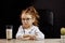 Gloomy little girl in spectacles refusing to drink milk, over black backgrounf