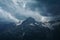 Gloomy mountain top landscape with thunder cloudy sky, rocky ranges and peaks with glaciers and snow fields