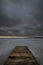 gloomy severe winter vertical gray landscape. an old wooden boardwalk pier on a large frozen lake under a thick dramatic cloudy