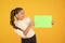 Glorious colour. Little girl holding empty sheet of paper on yellow background. Small child with blank green school