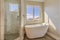 Glossy bathtub and separate shower inside the sunlit bathroom of a new house