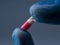 A gloved hand holds a capsule of medicine close-up. A doctor in a blue rubber glove. Blue background, copyspace.