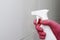 A gloved hand sprays a cleaning agent from the bottle onto a white tiled wall