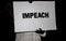 Gloved hands of person in winter coat holding IMPEACH sign at night-time rally