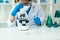 A gloved scientist pours blue acid into a test tube with clear liquid. Scientific research