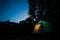 Glowing blue tent in the forest under a starry evening sky.