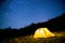 Glowing camping tent in the night mountain forest under a starry sky