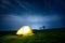 Glowing camping tent in the night mountains under a starry sky